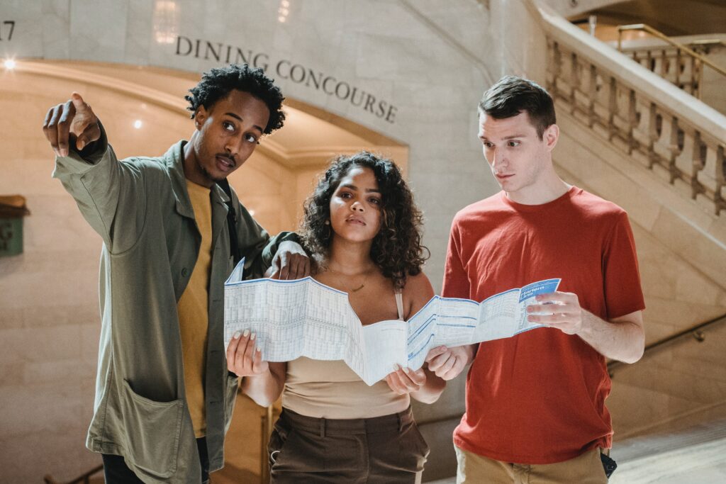 Concentrated young friends with map in a railway station: outsourced functions