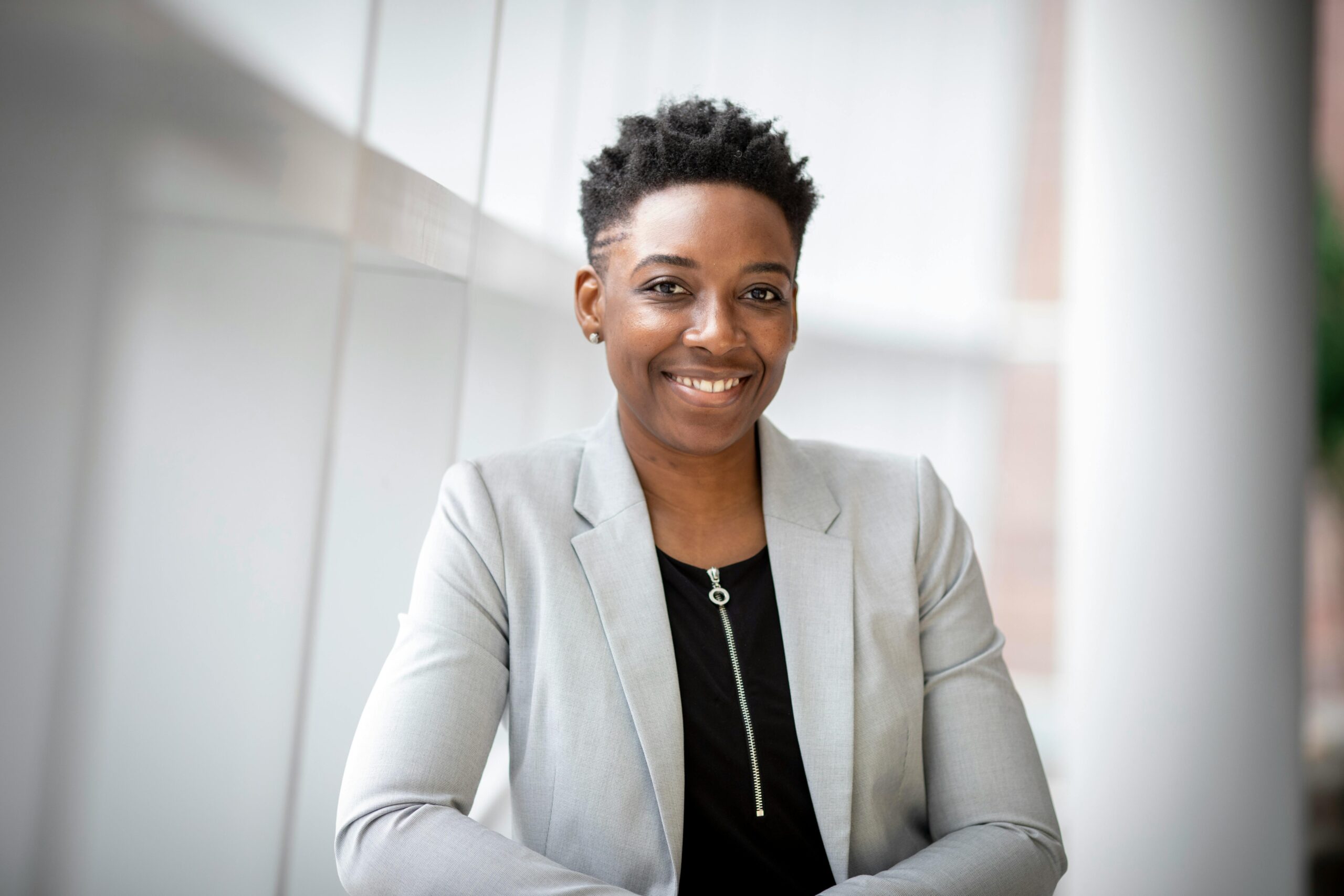 A smiling woman wearing a grey notch lapel suit jacket: outsourced communications