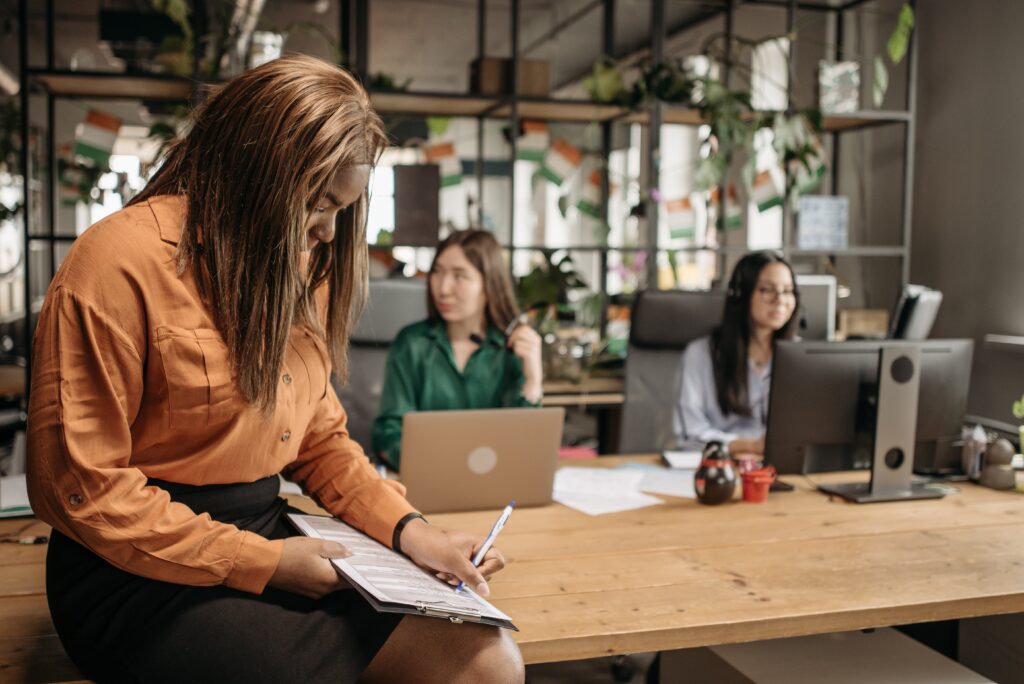 A woman in an orange button up shirt writing on a white paper: outsourced call centre