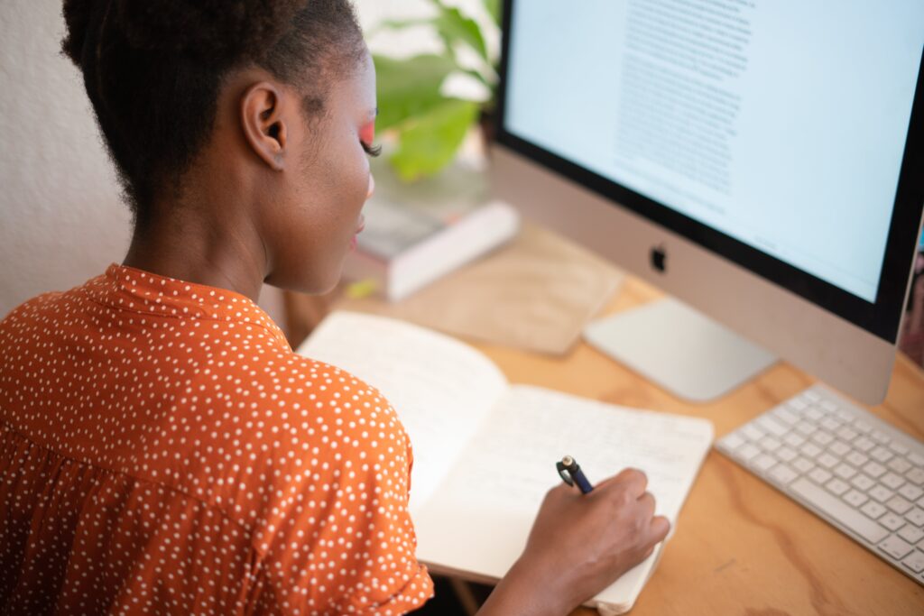 A woman sitting at a desk writing in a notebook: outsourced project manager